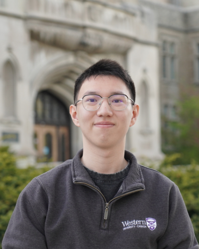 A student smiling in front of a brick wall with a sweater on